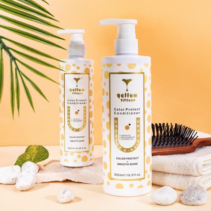 Two pump bottles of Yellow Titten Color Protect Conditioner with yellow polka dots sit on a peach background, surrounded by a palm frond, a hairbrush, towel, and white stones.