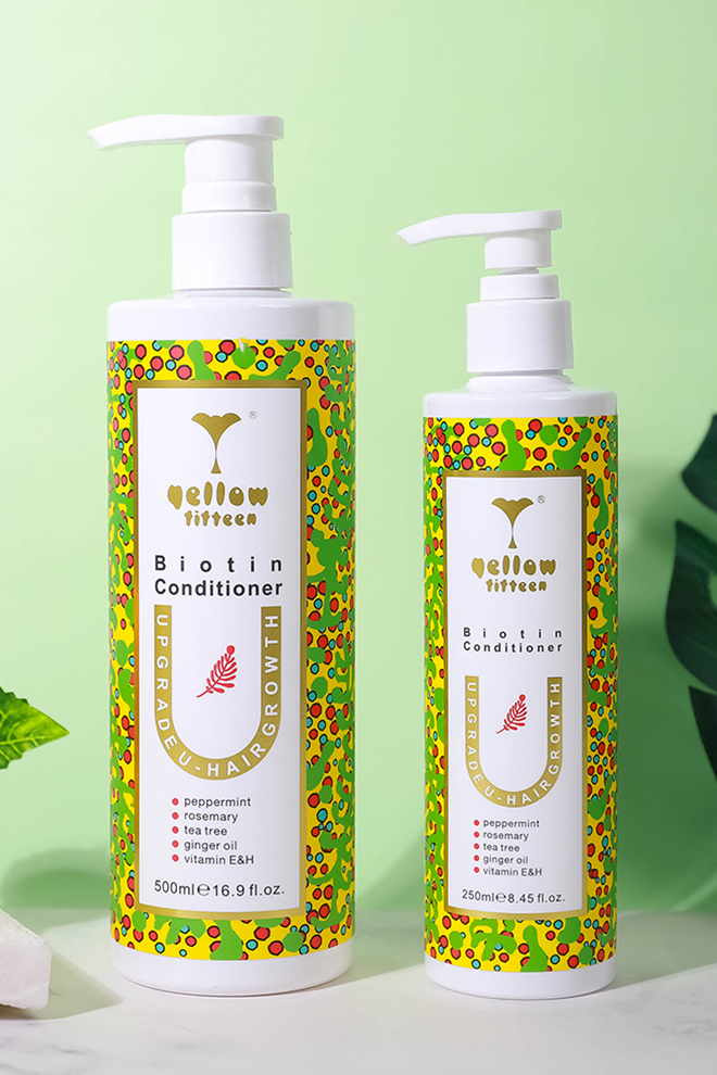 Two white bottles of biotin conditioner with bright, multicolored wrap labels on a pale green background (500 ml and 250 ml).