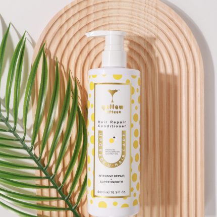 White conditioner bottle with a yellow polka-dot design and pump, labeled 'Hair Repair Conditioner' on a wooden tray with a green leaf beside it