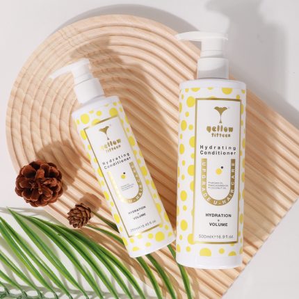 Two White bottles with yellow polka dots labeled 'Yellow Fifteen Hydrating Conditioner' on a wooden tray, with pinecones and green leaves nearby.
