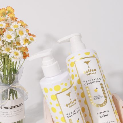 Two white pump bottles with yellow polka dots labeled Hydrating Conditioner, beside a vase of white and yellow daisies.-explanatory product shot