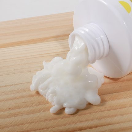 White toothpaste oozing from a tube onto a wooden surface on a counter.