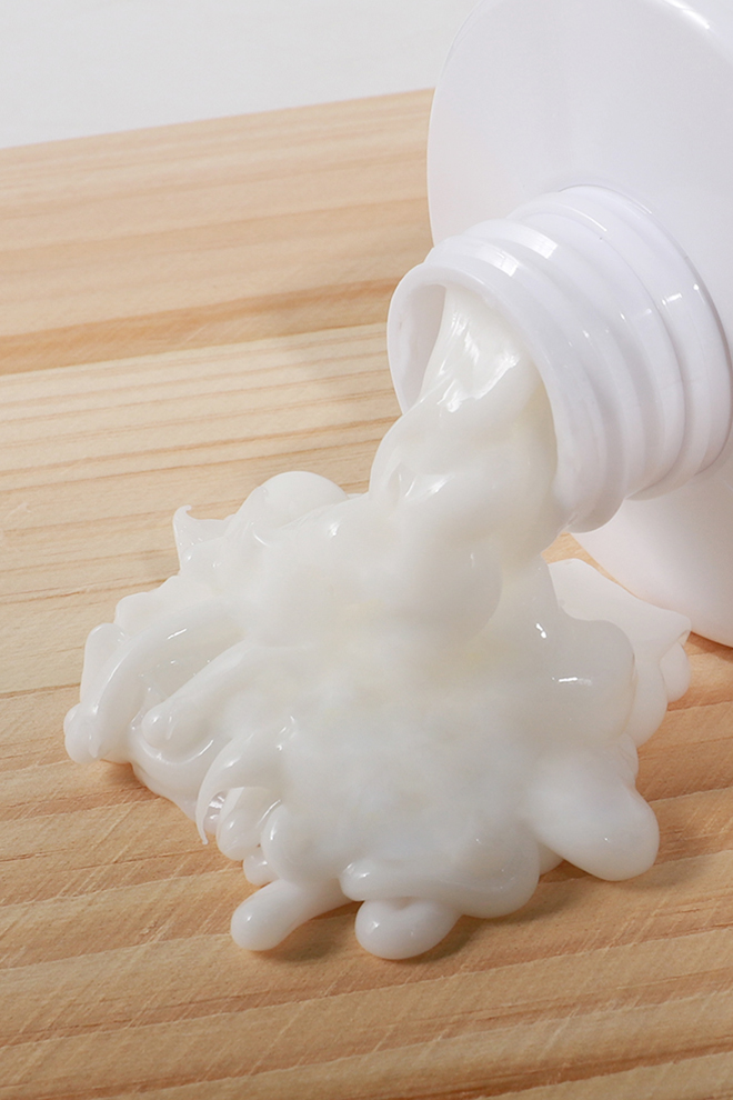 White lotion pouring from a tube onto a wooden surface, forming a glossy puddle on the table