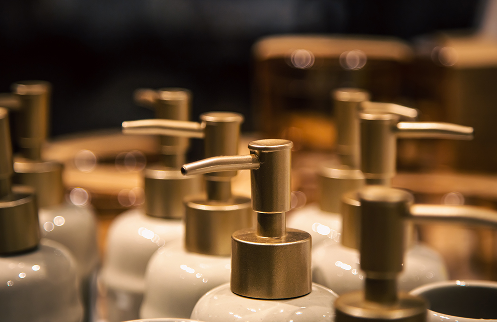Close-up of metal pump dispensers on white lotion bottles in a row, with shallow depth of field blur in the background.