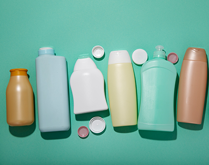 Row of assorted plastic cleaning bottles with caps on a turquoise background; colors include orange, light blue, white, pale yellow, green, and brown, with some caps loose nearby.
