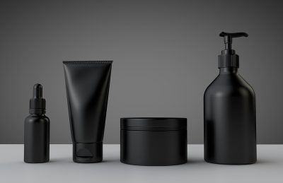 Set of matte black skincare containers on a gray surface: dropper bottle, squeezy tube, jar, and pump bottle in a row.
