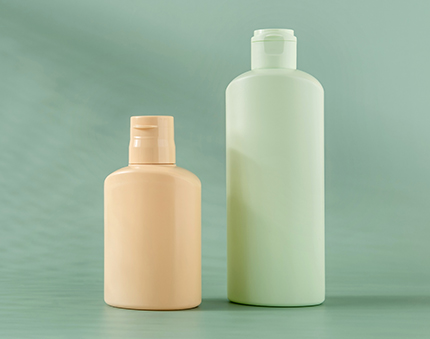 Two pastel plastic bottles, one small beige and one tall green, on a green backdrop (bathroom/beauty product setup).