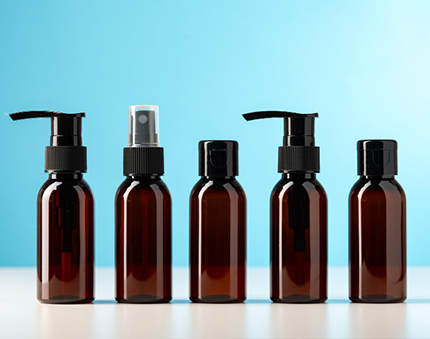 Line of five brown glass bottles with pump and spray tops on a white surface against a blue background