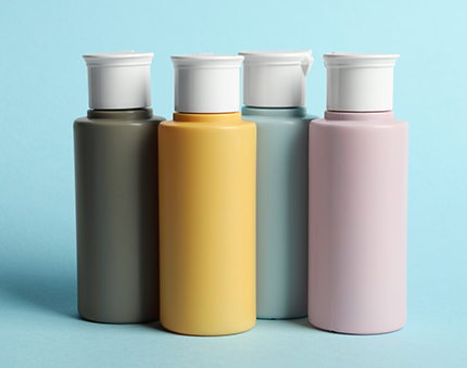 Four pastel paint bottles with white caps in olive green, yellow, teal, and pink, lined up on a light blue background.