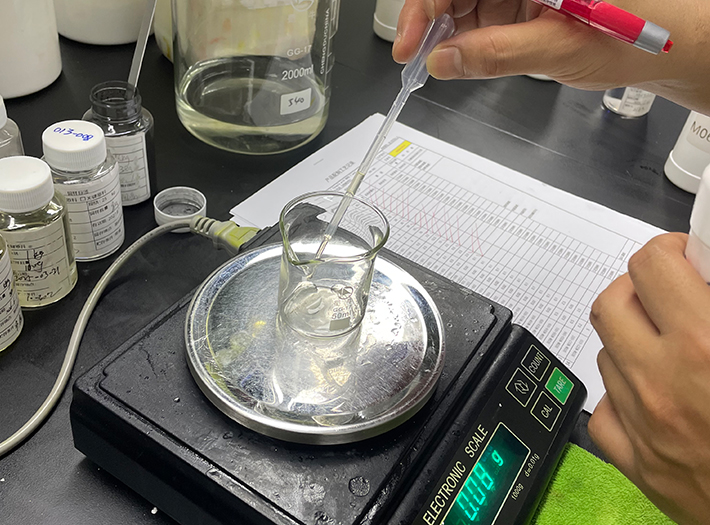 Scientist uses a pipette to add liquid to a small beaker on an electronic balance in a lab setting.